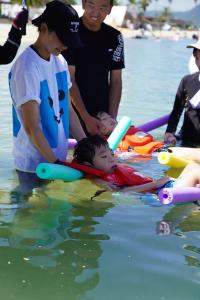 補助器具とボランティアの支えで海に入っている写真