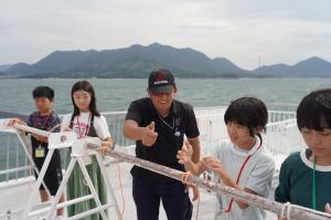 船のデッキでロープワークをする子どもたちの写真